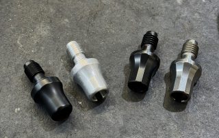 Four Defiance Machine bolt shrouds in black and raw metal finishes, showing smooth tapered and faceted profiles
